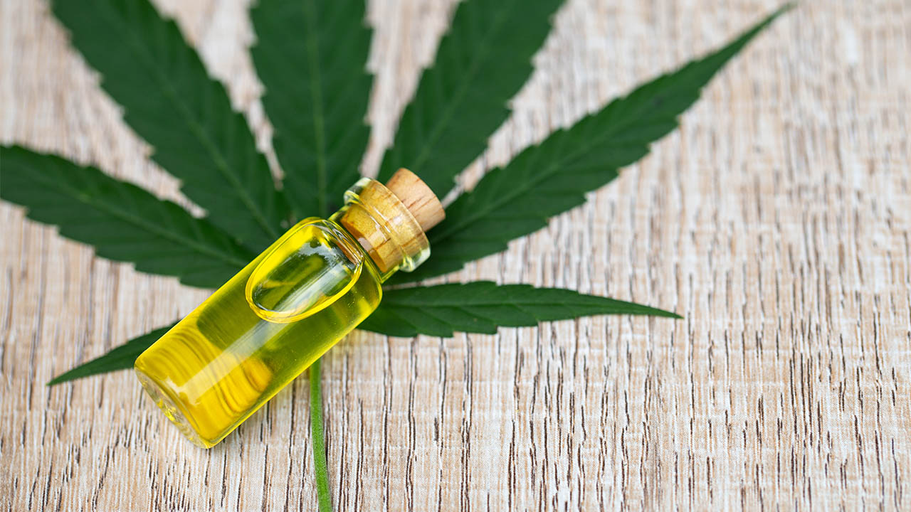 Bottle of CBD oil laying over a cannabis leaf